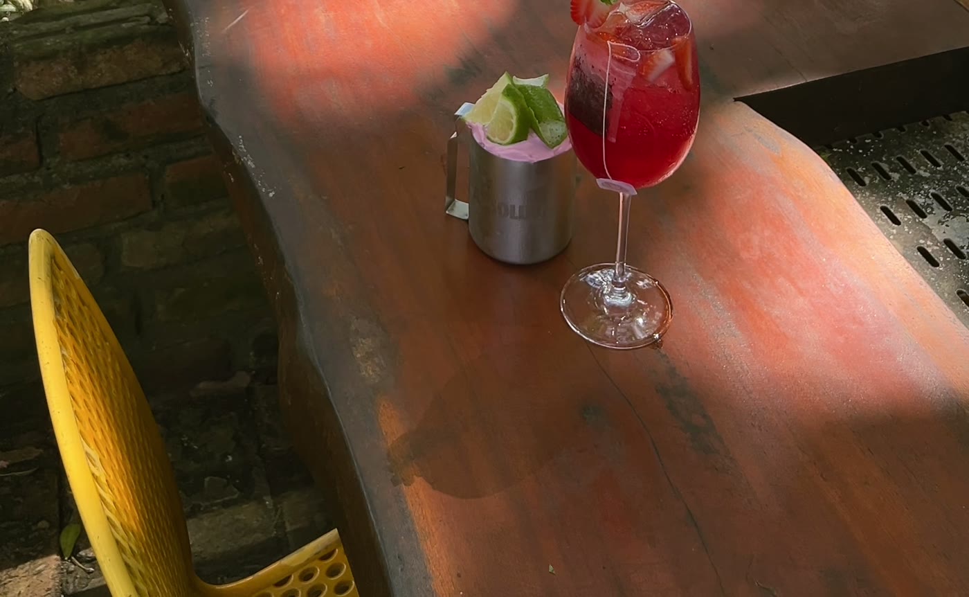 Drink servido na mesa de madeira do terraço no fim da tarde, com a luz do sol atravessando as folhas.